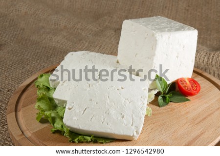 White cheese with some garnitures such as lettuce, a slice of cherry tomato and bassil on a wooden plate with sackcloth table sheet