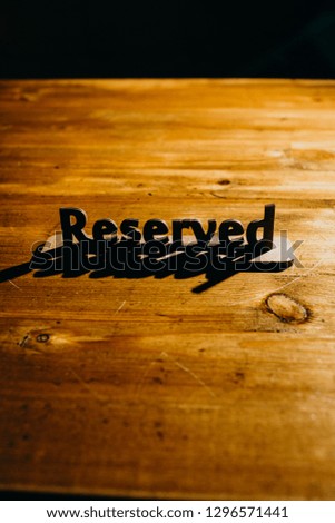 
wooden plate "reserved" on a wooden table in hard light