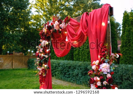 Wedding. Ceremony. Wedding arch. Red wedding arch of flowers and greenery stands on the green grass in the park.