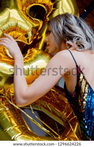 Young woman with golden balloons on her thirty years birthday. Indoor location. Person is in vintage 80th dress and hairstyle. At home