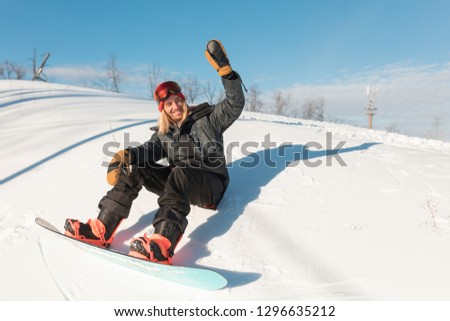 cheerful sporty man is greeting somebody while sitting on the snowy peak. copy space. full length photo. gesture.