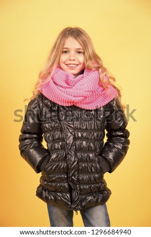 Child model smile with long blond hair. Girl in black coat and pink scarf on orange background. Kid beauty, look, hairstyle. Autumn fashion, style, trend. Happy childhood concept.