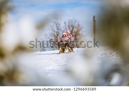 Two girls, twin sisters sledging downhill on snow covered mountain trail. Winter fun vacation.