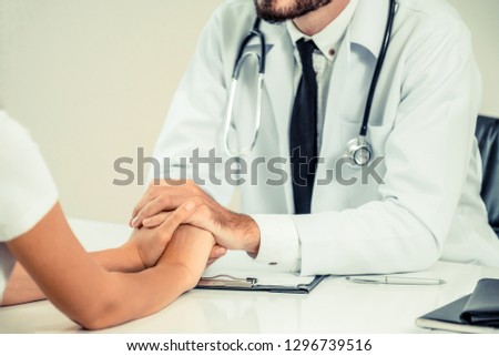 Male doctor soothes a female patient in hospital office while holding the patients hands. Healthcare and medical service.