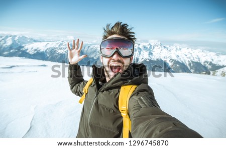 Handsome funny skier is taking a selfie at wintertime in the snow on a mountain