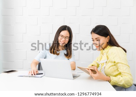 Shot of two young, beautiful, Asian architects, discuss project planning, taking note on notepad, pointing at notebook and tablet, comparing and sharing information, with white brick wall background