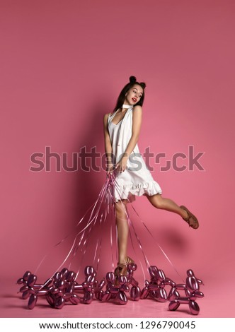 Young beautiful girl in white dress walk the inflatable balloon dogs on a leash happy smiling on pink background