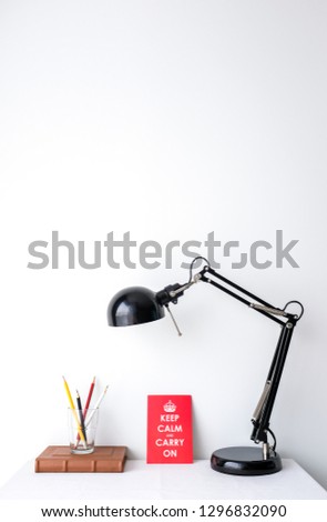 Retro black desk lamp  a glass of sharp pencil a brown vintage notebook a motivational quote poster on white table top on white wall background with copy space product mock up placement