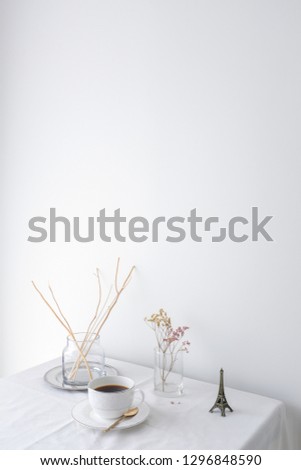 Glass vase of dried flower plant an eiffel tower miniature on white table top on white wall background with blank copy space for product mock up placement 
