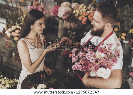 A young girl pays for the purchase of a flower. A beautiful smiling girl is paying by credit card for buying fresh flowers for a gift to a young bearded flower seller. Flower business concept.