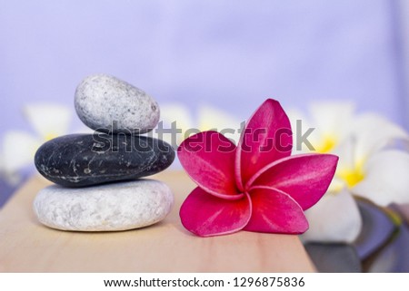 Holistic health concept of zen stones with deep red plumeria flower on wooden board.