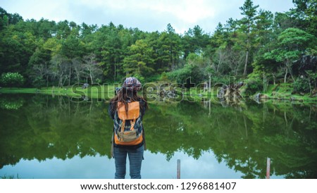 Young women travel nature. She stands waterfront at the public park Photographing beautiful landscape.
