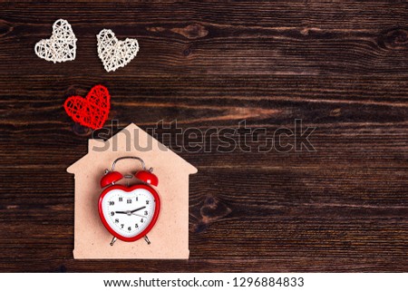 Alarm clock with home symbol and hearts on wooden background. Valentine's day concept. Top view.