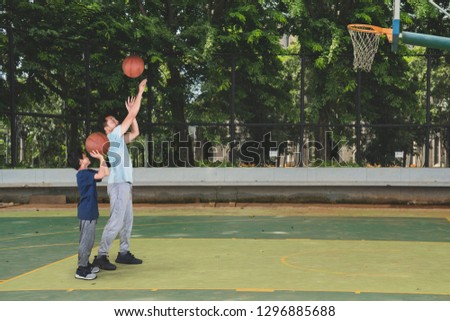 Picture of little boy learning to shoot a basketball with his father while exercising in the court