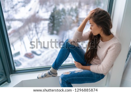 Winter depressed sad girl lonely by home window looking at cold weather upset unhappy. Bad feelings stress, anxiety, grief, emotions. Asian woman portrait. Royalty-Free Stock Photo #1296885874