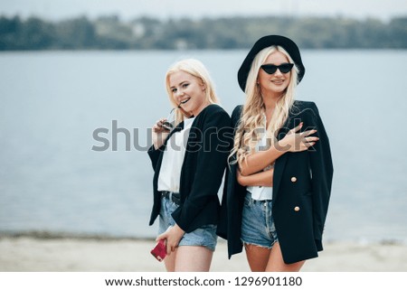 Two pretty girls blondes in glasses walking along the coast, talking and enjoying life