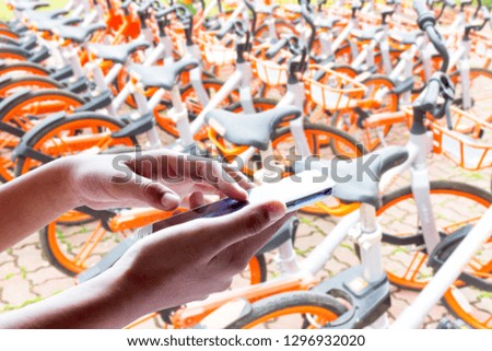 Man use mobile phone, blur image of bicycle for rent as background.