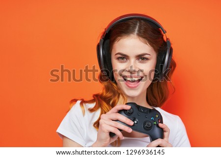 Happy teenager in headphones on an orange background holding a joystick in his hands and smiling                         