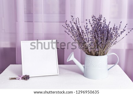 Lavender flowers in watering can and photo frame (mock-up) on window with tulle cloth background, copy space.  Soft focus. 