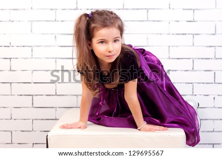 5 year old girl in a purple dress next to a white brick wall
