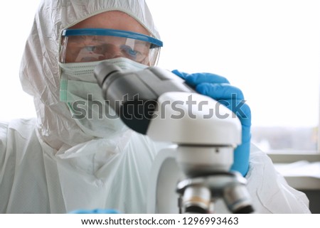 Male chemist in blue protective gloves look at microscope in chemistry lab backround portrait. Studies viral effect biological contamination human behavior dna human eco reproduction cells concept