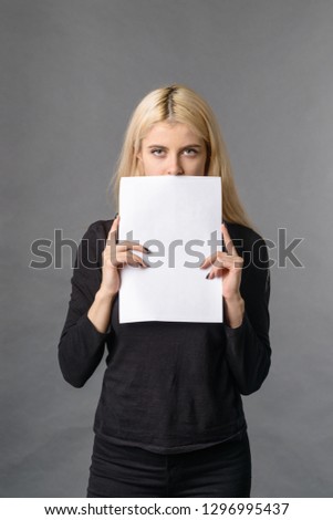 Nice pretty blonde female hides her face behind white banner blank white sheet mockup for copy space