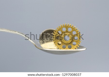 coin and gear in teaspoon on grey background, uniform background