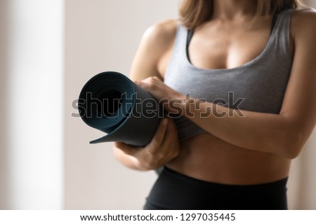 Close up of toned young woman wear sportswear hold yoga mat in hands stand ready for workout in gym, fit female athlete in sport bra prepared for pilates class in fitness studio. Healthy life concept
