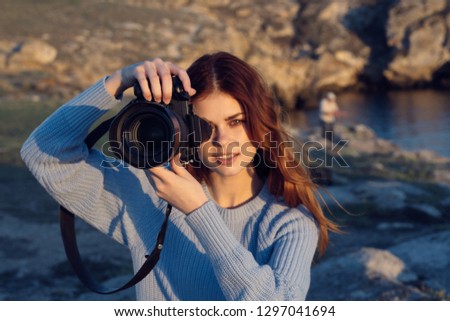 Cute red-haired woman in a blue sweater with a camera on the nature