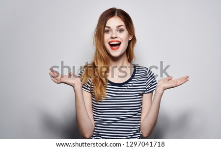 Cheerful woman in a striped T-shirt spreads her arms against a gray background