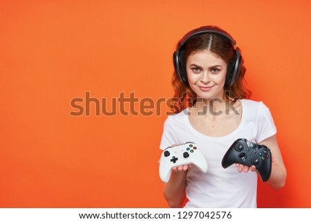 Pretty woman gamer with controllers in her hands and in headphones on an orange background