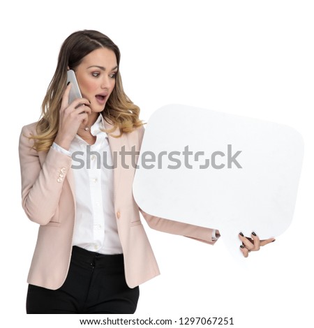 surprised businesswoman talking on the phone looks to side at speech bubble with mouth open while standing on white background