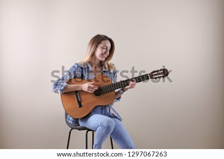 Young woman playing acoustic guitar on grey background