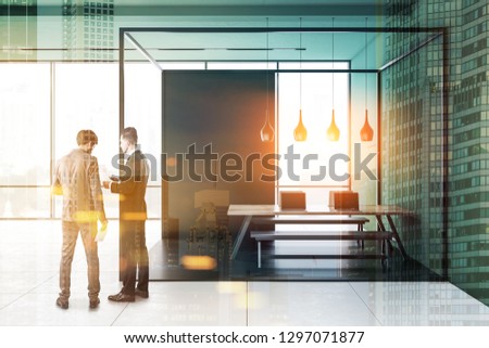 Two businessmen talking in original panoramic office interior with green walls, tiled floor and long wooden table with benches standing in black and glass room. Toned image double exposure