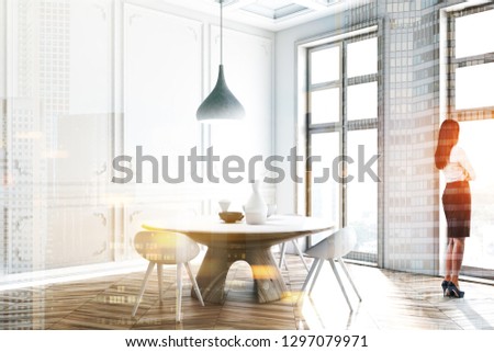 Woman in corner of luxury dining room with white walls, wooden floor, tall windows and round table with white chairs. Toned image double exposure