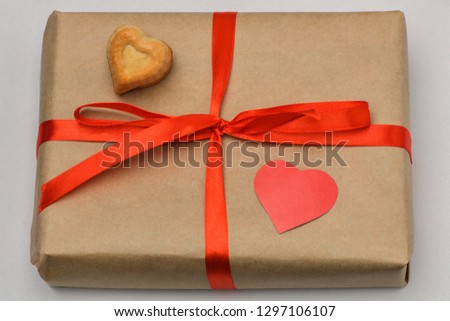 Hearts made of paper. Valentines day. The gift box on a gray background in a Kraft brown package is tied with a red ribbon and on top is one carved red heart and one heart-shaped cookie