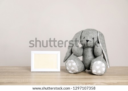 Photo frame with space for text and adorable toy bunny on table against light background. Child room elements
