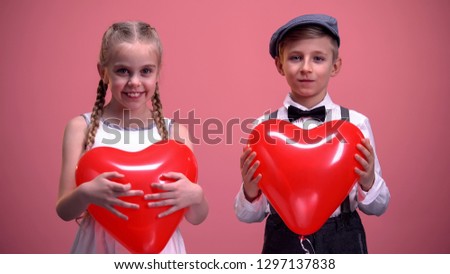 Cheerful kids in love holding red heart-shaped balloons and smiling to camera