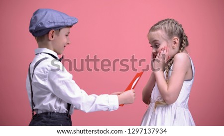 Little boy in formal wear presenting birthday gift card to happy surprised girl