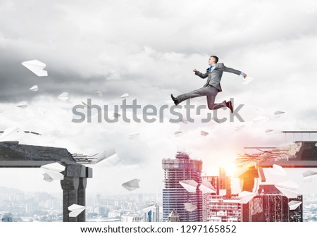 Businessman jumping over gap with flying paper planes in concrete bridge as symbol of overcoming challenges. Cityscape with sunlight on background. 3D rendering.