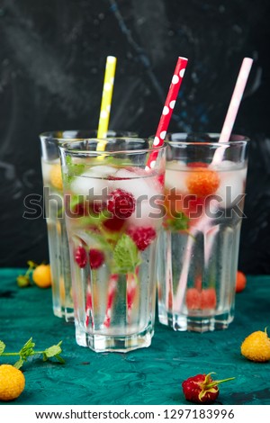 Detox infused flavored water with three color raspberry - red, orange, yellow on green background. Refreshing summer homemade cocktail