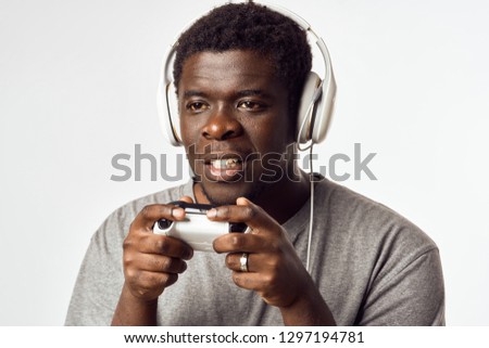 a black man plays on the game console with a joystick in his hands and headphones