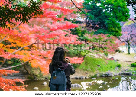 Young Asian women tourist standing before a pond and seeing autumn leaves in Japanese garden (Tokyo, Japan)