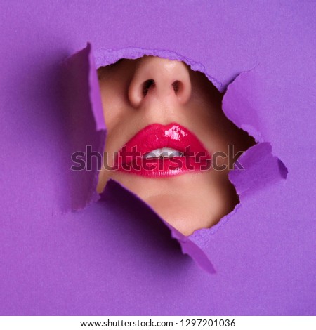 View of bright lips through hole in violet paper background. Make up artist, beauty concept. Cosmetics sale. Beauty salon advertising banner with copy space. Square crop.