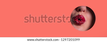 Beautiful red lips giving kiss through hole in living coral paper background. Make up artist, beauty concept. Cosmetics sale. Beauty salon advertising banner with copy space.