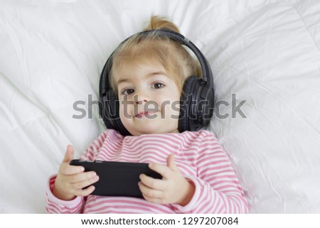 Little girl lying with headphones and smartphone.