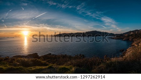 There is a panoramic picture with a sunset near the sea on a small bay.