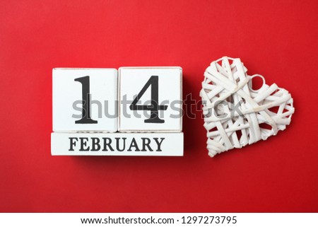 Wooden calendar with date of February 14 and white decorative heart on bright red background. Concept Valentine's day, love.