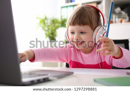 Satisfied child in headphones sitting at home office table and looking laptop monitor. Makes orders online store with home delivery push button keyboard concept management game play early development