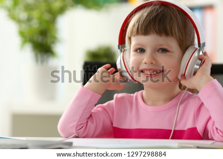 Satisfied child in headphones sitting at home office table and looking into camera portrait. Makes orders in online store with home delivery concept management game play early development